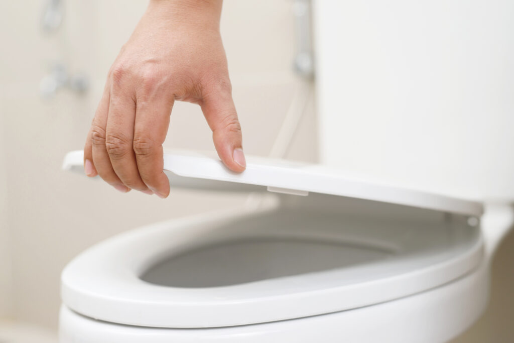 A hand is lowering the lid of a white toilet in a bathroom setting.