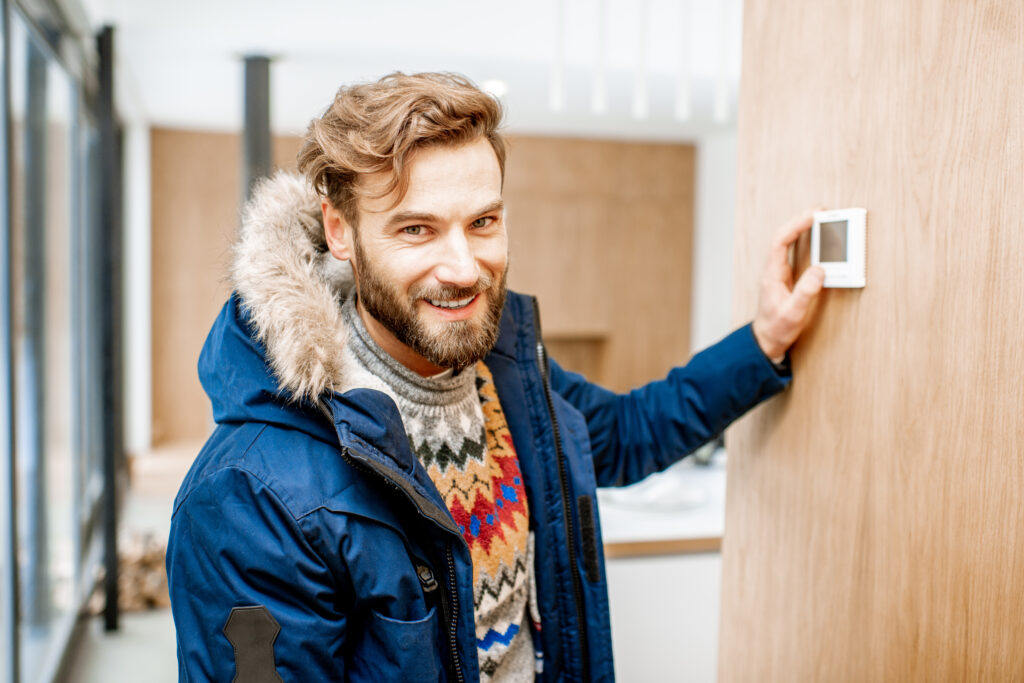 Man in winter clothes feeling cold adjusting room temperature with electronic thermostat at home